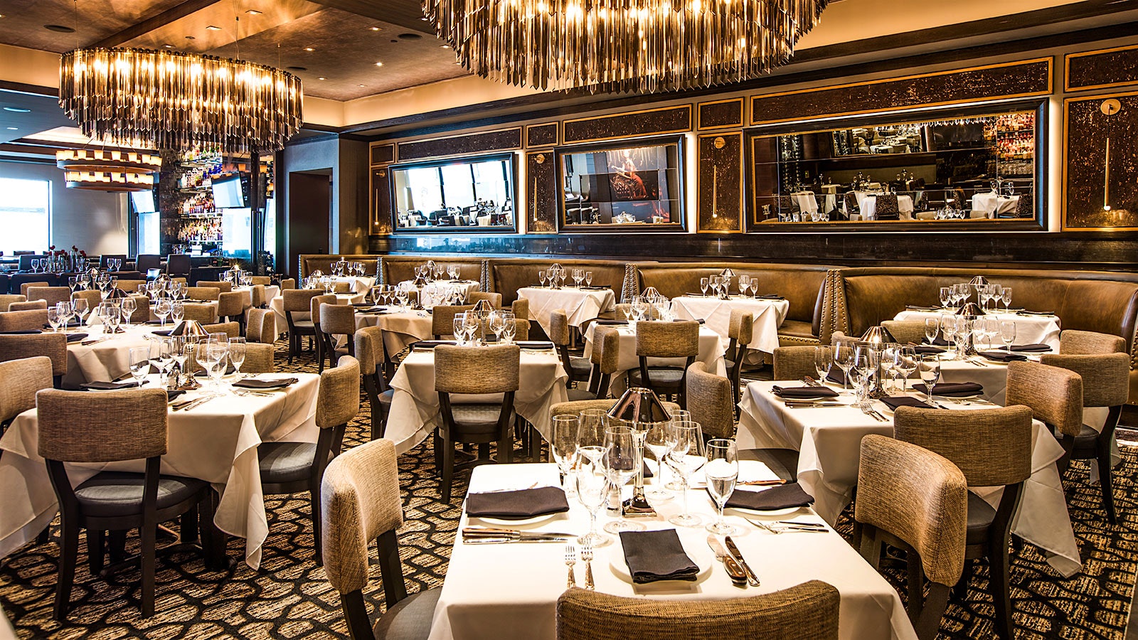 A modern-style dining room at Mastro’s at the Post Oak Hotel, with beige chairs and a large wine fridge full of bottles, stretching across the wall
